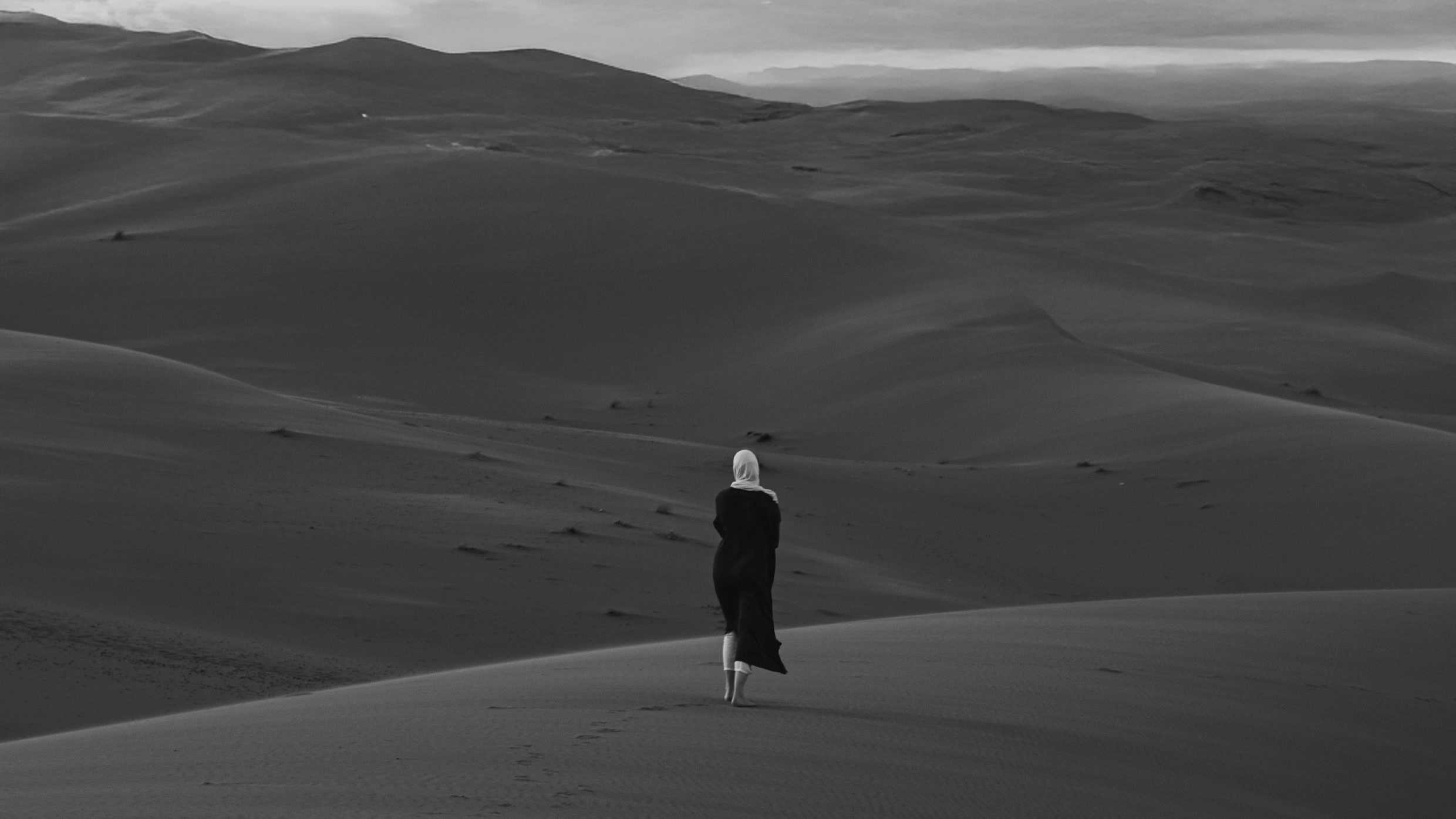 Professional artistic portrait photography of a woman in a hijab standing alone on desert sand dunes, showcasing dramatic black and white landscape photography by Cmone Creative Sweden
